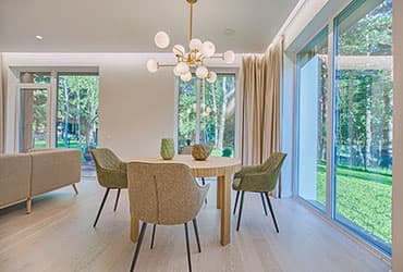 Sala de jantar de uma casa, com mesa de madeira, cadeiras estofadas e portas de vidro abertas para o jardim